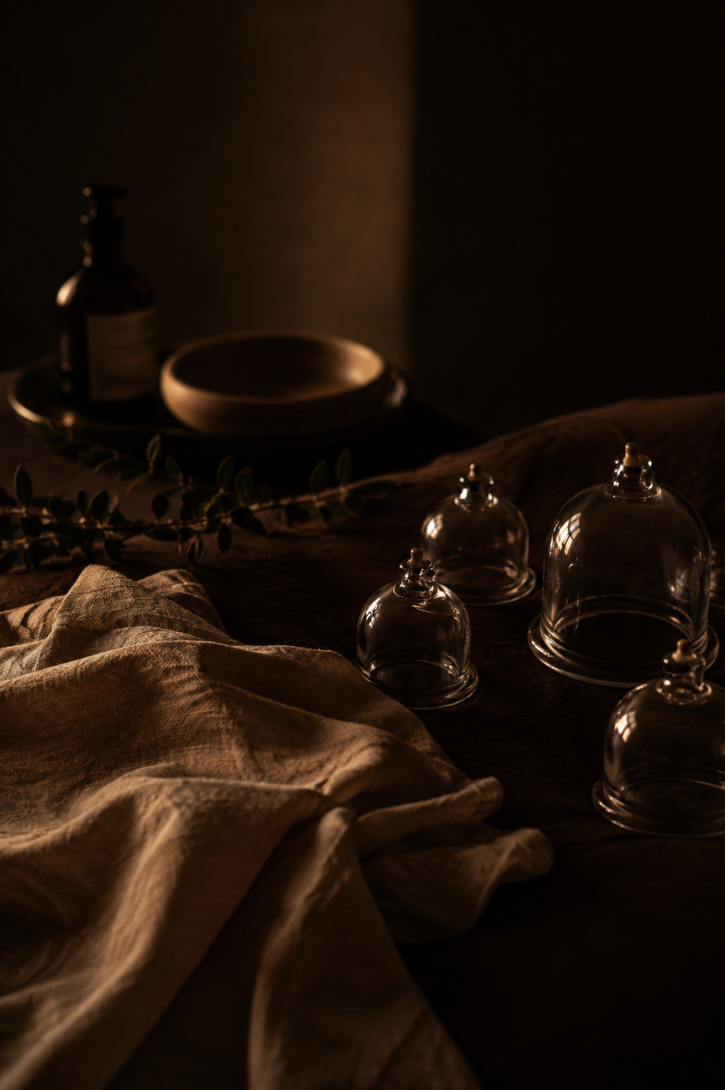 Glass cupping cups, linen and massage oil arranged in warm low light
